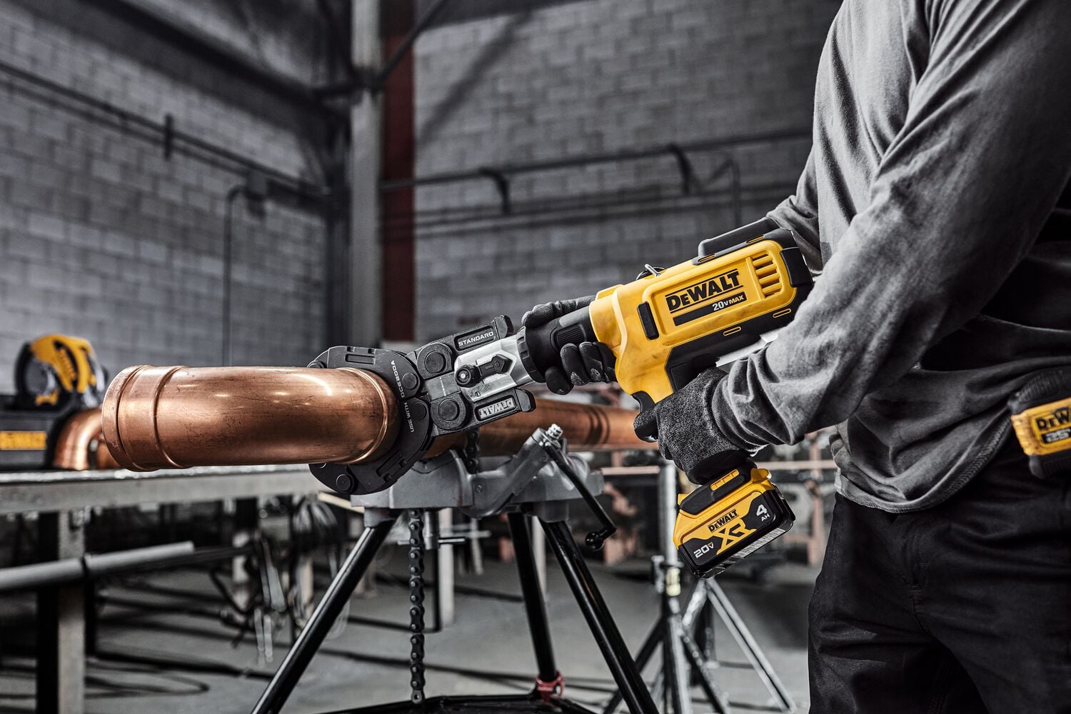 A person using a yellow and black DEWALT branded power tool to clamp or press a large copper pipe in an industrial or workshop setting.