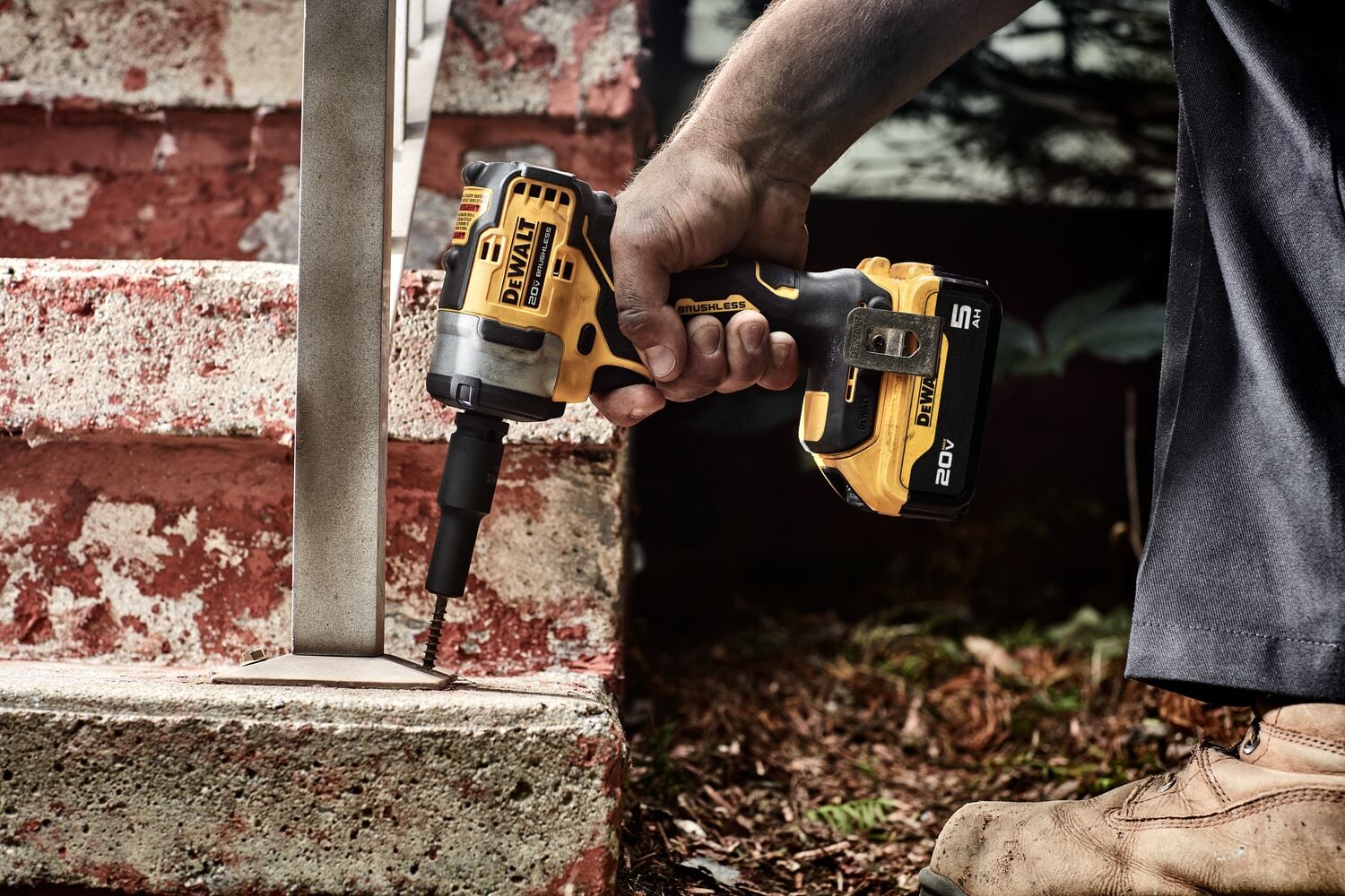 A person using a DEWALT 20V cordless impact wrench to fasten a metal bracket to a concrete step outdoors.