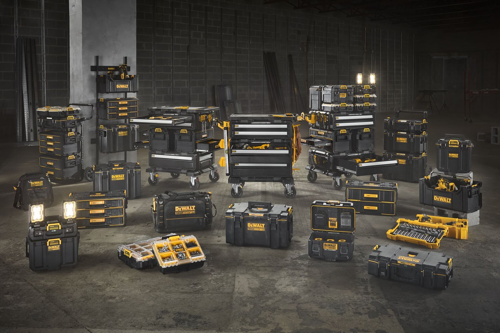 A large assortment of DEWALT storage and toolboxes, including rolling tool chests, organizers, tool cases, and portable workshop units, are arranged in an industrial warehouse setting. The products are mostly black with yellow accents and various sizes.