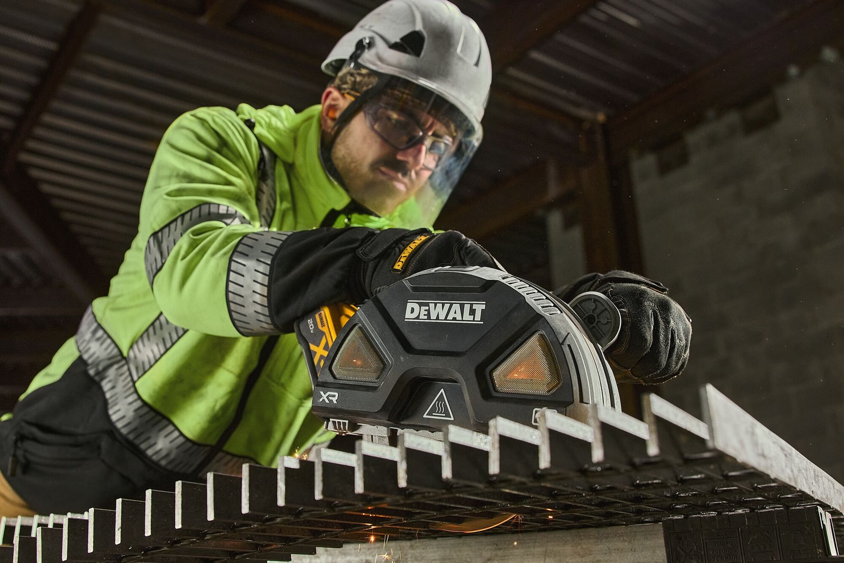 A person wearing safety gear such as a helmet and gloves is using a DEWALT branded power tool to cut through a metal grate at an industrial worksite.