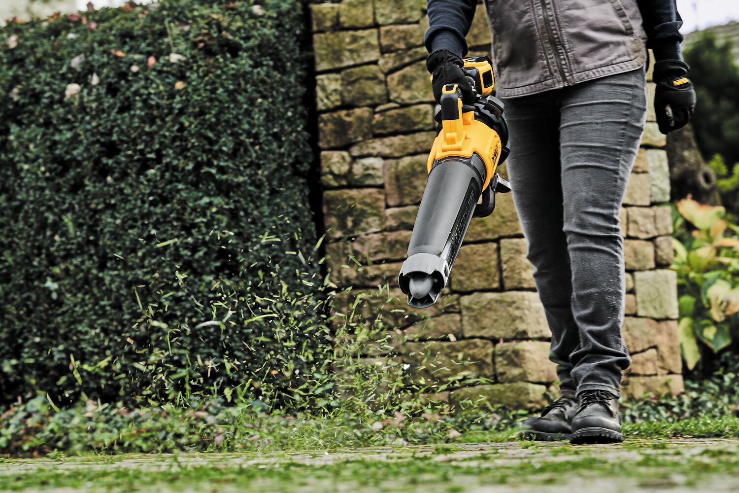 LITHIUM ION XR® Brushless, handheld blower with nozzle being used by a person to blow grass blades off ground.