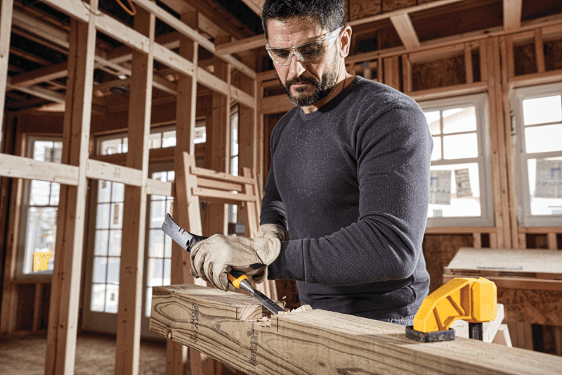 3 quarters inch Wood Chisel being struck with hammer by worker to scrape wooden log surface at worksite.